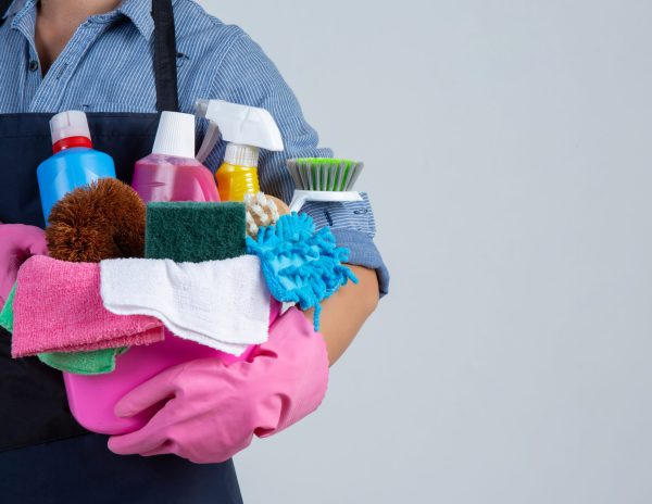 Young girl is holding cleaning product, gloves and rags in the basin on white background